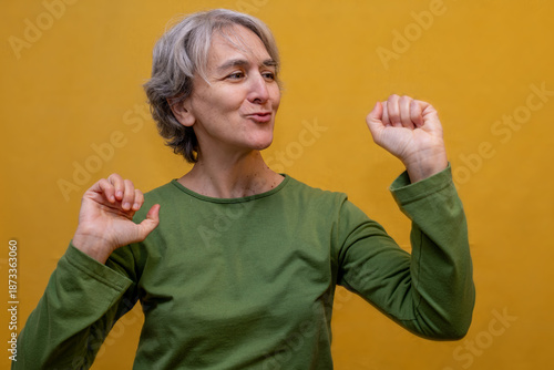 Принти на полотні Energetic senior woman with gray hair dancing enthusiastically against a yellow