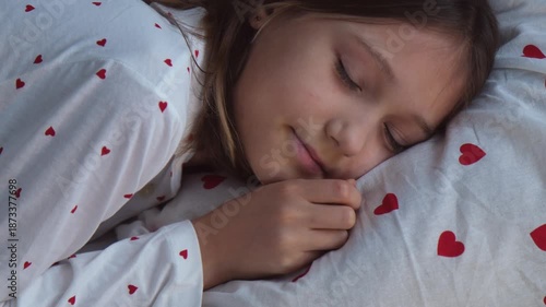 A little girl sleeps sweetly in pajamas with hearts, adjusting her pillow more comfortably.