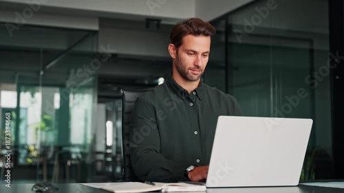 Focused business man salesman working on laptop computer reading financial contract document, writing notes in office. Young manager businessman specialist doing paperwork analysing on pc. Copy space