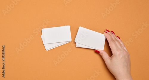 A woman's hand holds a stack of blank white business cards against a rich orange background.