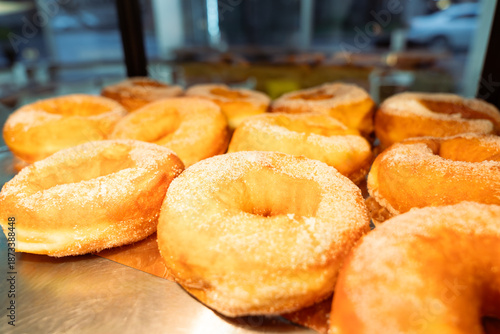 Freshly fried sugar-coated donuts displayed on metal counter, showcasing golden texture and bakery freshness.