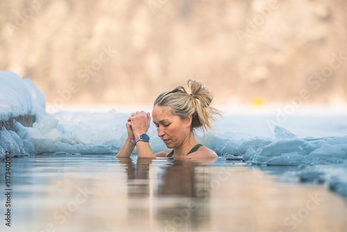 Beautiful blonde hair woman immersed in the freezing cold water of a lake practicing cold water swimming. Wim Hof Method, cold therapy, breathing techniques, yoga and meditation