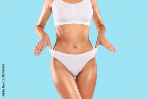 Wallpaper Mural Close up shot of unrecognizable fit woman wearing lingerie pulling up white panties standing isolated on blue studio background. Torso of slim female with flat belly in underwear top bra Torontodigital.ca