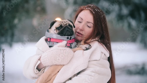 The pug is shivering from the cold. A worried young woman hugs her dog to keep warm on a frosty day outside.