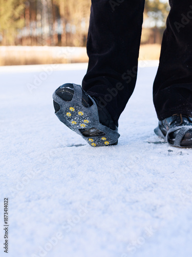 Model wearing winter traction cleats walking on snowy icy surface outdoors.Concept of winter walking safety, fall prevention, outdoor mobility, product demonstration.