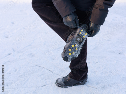 Man fastening winter traction cleats on boot while standing on icy surface.Concept of step-by-step product use, winter safety instruction, outdoor gear.