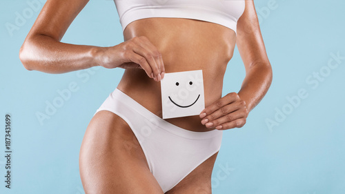 Love Yourself, Body Positivity And Care Concept. Closeup cropped view of unrecognizable slim woman holding paper post-it sticker note with smiley face over blue studio background, banner, panorama