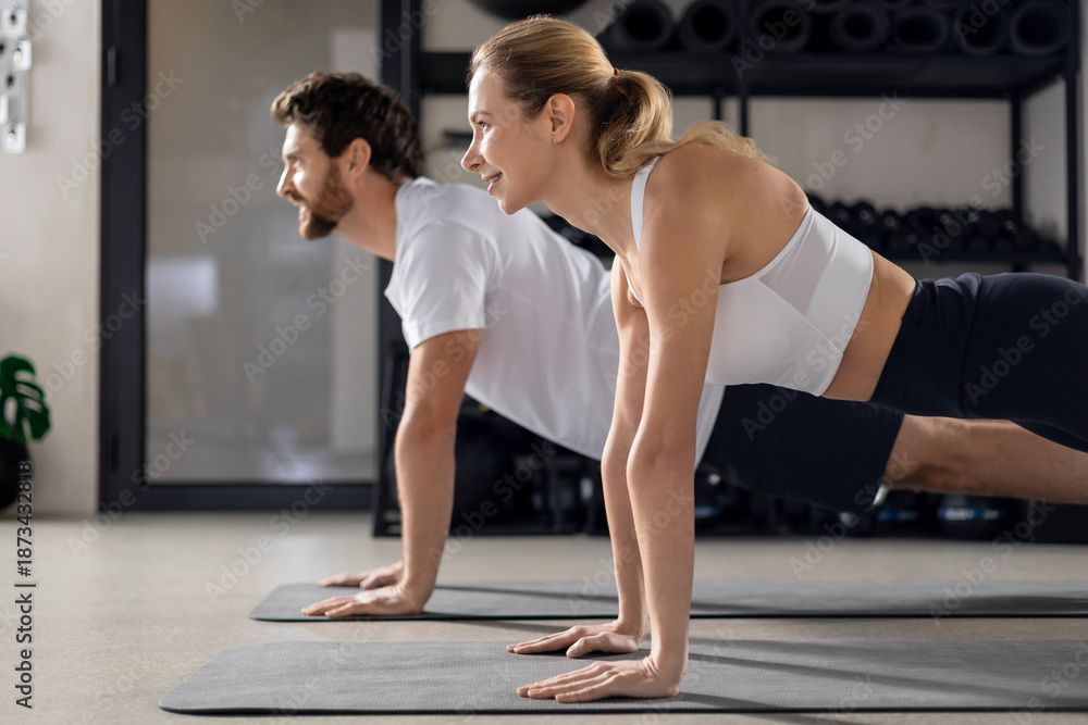 Fototapeta premium Two people having a workout in gym and standing in plank