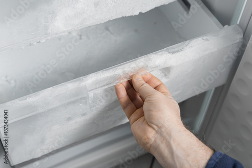 Schilderij op canvas Man defrosting refrigerator drawer with ice buildup and frozen food