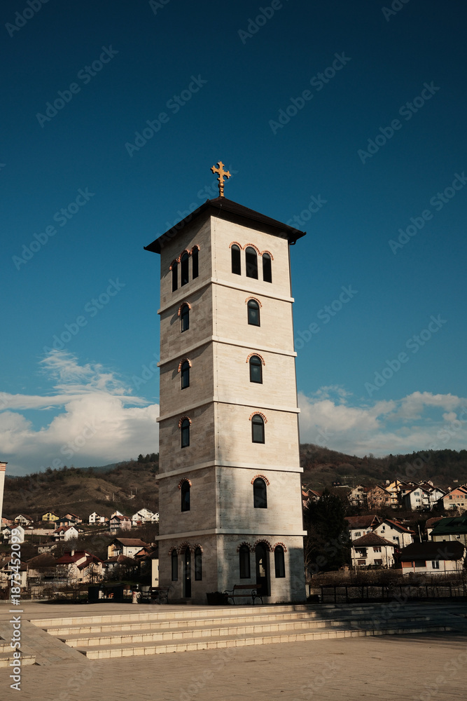 Fototapeta premium Tall stone bell tower rising above Andricgrad in Visegrad, Bosnia and Herzegovina. Vertical structure represents tradition, religion, and historical continuity.