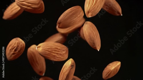 numerous perfectly formed raw brown almonds gracefully falling, tumbling in super slow motion, medium close-up, against a pure deep black void with soft bokeh, strong studio lighting, high-end food