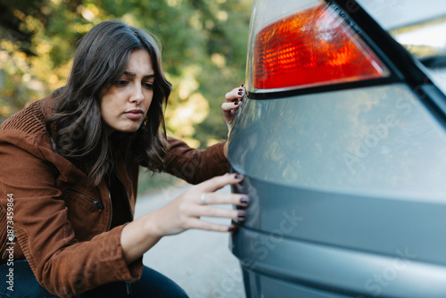 Fotografi Frustrated young woman looking at scratch on her car