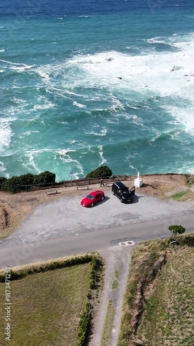 Aerial view of a rugged coastline revealing the scenic Cabo Vidio lighthouse in Asturias, Spain, with waves crashing against the cliffs