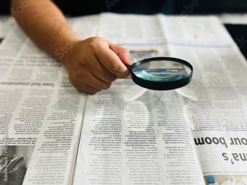 Εκτύπωση καμβά A person's hand moves a magnifying glass over a printed newspaper to read fine print, symbolizing investigative journalism, research, information seeking, or vision assistance