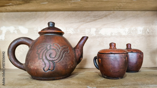 Traditional handmade clay teapot and cups displayed on a wooden shelf, showcasing rustic pottery craftsmanship. Vintage ceramic teapot set with cups,