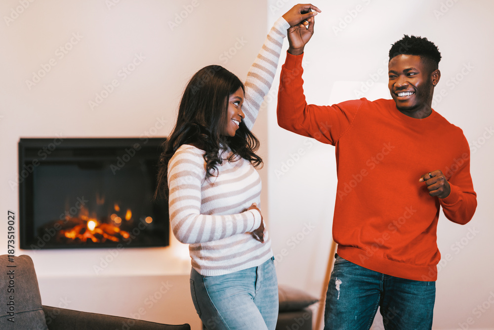 Obraz premium A couple enjoys a fun moment, dancing together in a warm indoor setting with a fireplace. They are smiling and holding hands, clearly enjoying their time together.