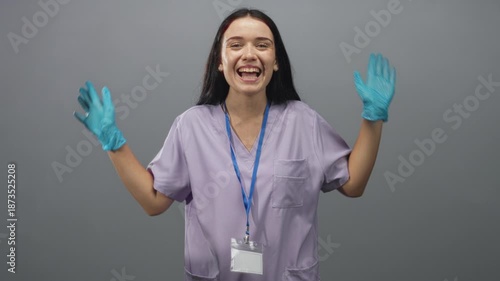 Nurse woman laughing with gloved hands raised and id badge visible in studio; joyful compassion teamwork support.