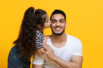 Love My Daddy. Cute Little Female Child Kissing Her Happy Arab Dad While They Posing Together Over Yellow Studio Background, Cheerful Middle Eastern Father Enjoying Time With His Daughter, Free Space