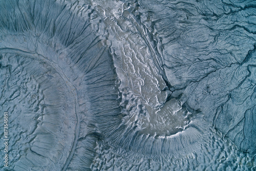 Abstract blue gray mudflow texture with deep cracks and frozen landslide patterns, cold industrial wasteland background aerial top down view