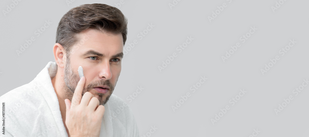 Fototapeta premium Banner of beauty male portrait of a beautiful man applying face cream. Moisturizing skincare cream for man. Mask for skin lifting and anti-aging effect. Beauty male face concept. Skincare and aging.