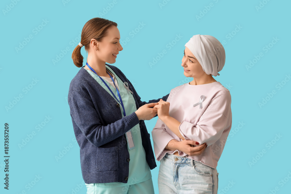 Fototapeta premium Young woman after chemotherapy with nurse holding hands on blue background. Brain cancer concept
