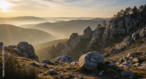 Rocky mountain terrain overlooks multiple receding ranges shrouded in morning haze bathed in golden light