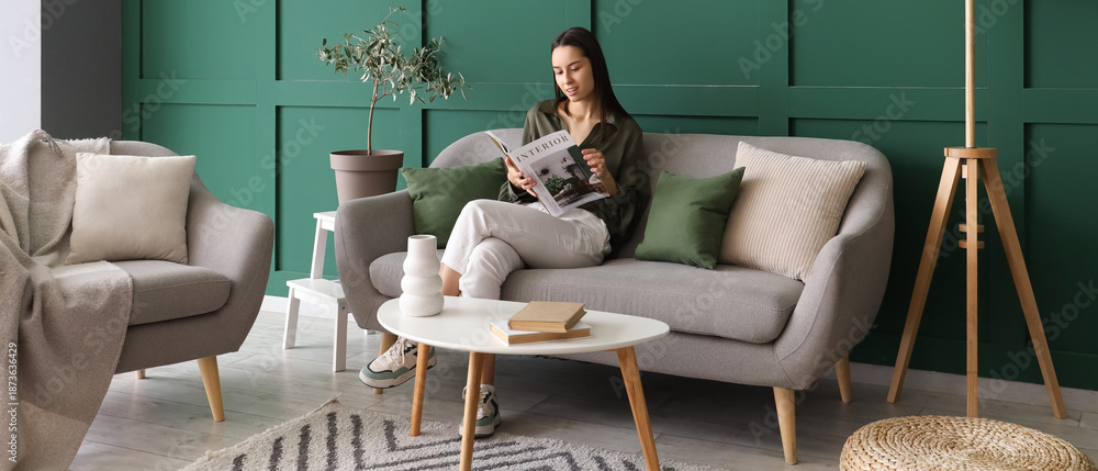 Fototapeta premium Beautiful woman reading magazine on grey sofa in living room