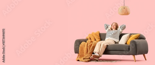 Young woman resting on stylish grey sofa against pink background with space for text