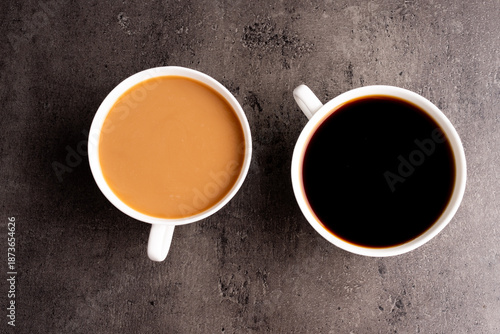 two cups of coffee on a kitchen bench one black one white with a wooden floor in the background