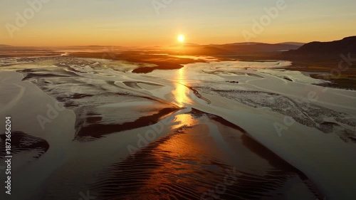 Sunrise at low tide, sun reflecting off black volcanic sand