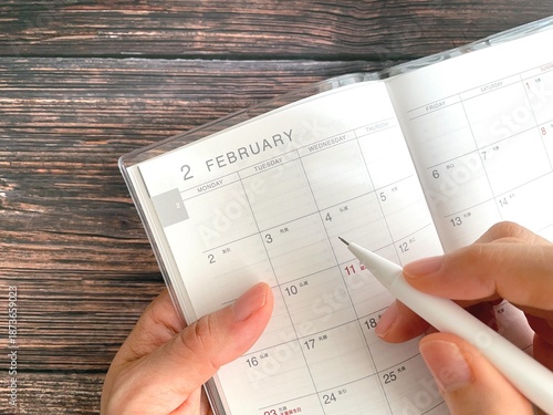 Cuadro en lienzo Woman's hand filling out February schedule book on wooden table