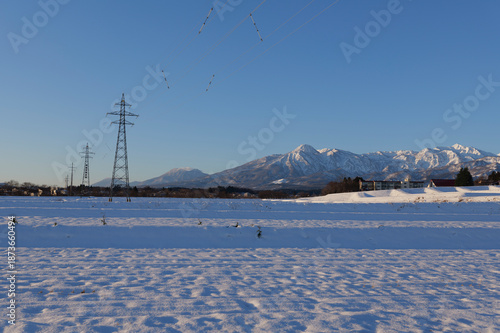 雪原に立つ送電鉄塔と遠くにそびえる冠雪の妙高山