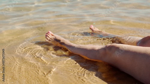 A woman's feet touch the sea water on a sandy beach. The girl is sitting on the sand with her feet in the sea water. A tropical vacation.