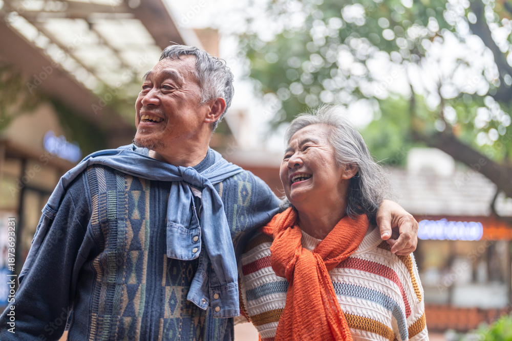 Naklejka premium Happy senior asian couple walking and laughing together outdoors, elderly husband and wife enjoying retirement lifestyle and travel in winter, active aging, insurance and health care concept