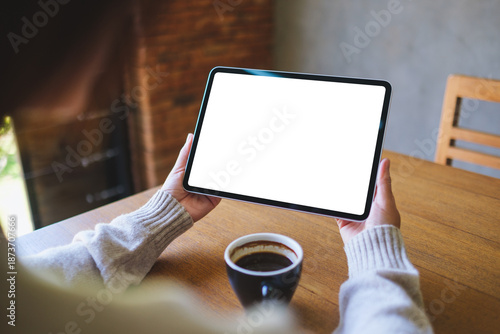 Mockup image of a woman holding digital tablet with blank white desktop screen in cafe