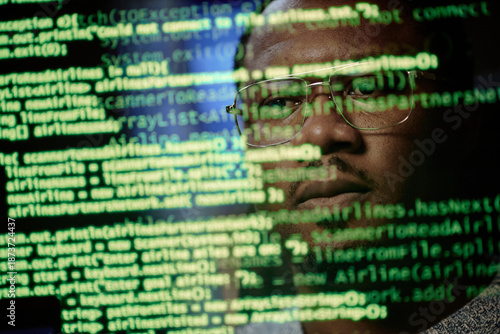 Fotografie Portrait of Black man wearing glasses looking at computer screen with lines of c