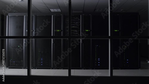 Dark server room with rows of computer servers behind glass panels in a modern data center with a cool and technological mood.