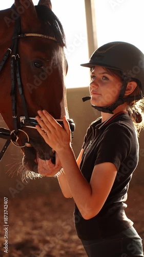Girl carefully adjusts horse's harness, showing care for it by touching it. Rider carefully places bridle on horse in arena in daylight. Girl carefully prepares horse for riding. Riding, love and care