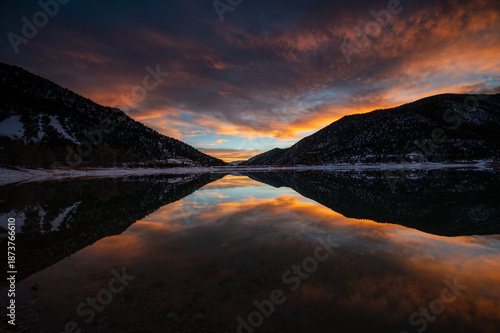 Intensely colorful sunset cloudscape over Grass Valley Reservoir in Harvey Gap State Park, Colorado reflected in reservoir's calm water.