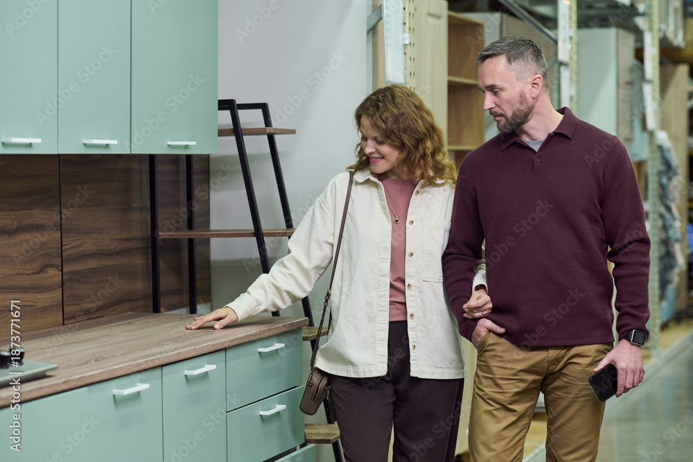 Fototapeta premium Couple walking together in store, examining kitchen cabinets and countertops, woman touching surface while man holding smartphone