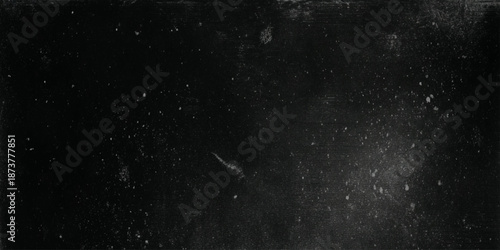 A dark grainy texture with scattered white specks and subtle light variations across the surface