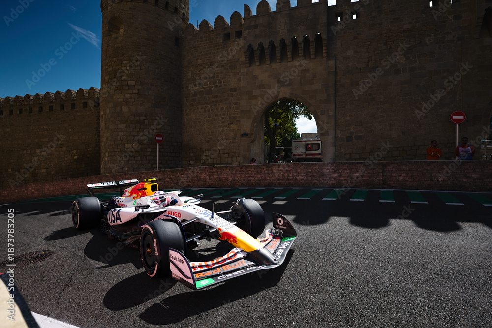 Naklejka premium BAKU, AZERBAIJAN - SEPTEMBER 20, 2025: A Visa Cash App RB Formula 1 car accelerates past the historic fortress walls of the Old City (Icherisheher) during the Azerbaijan Grand Prix