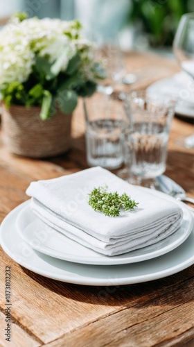 A sleek chrome napkin holder rests on a wooden table set with plates, glasses, and a small flower pot. The scene is prepared for a meal with guests