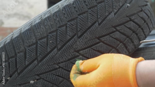 Driver hand in gloves removes dirt and stones trapped in tread. Road safety depends on proper grip. Winter readiness requires attention to detail before cold weather