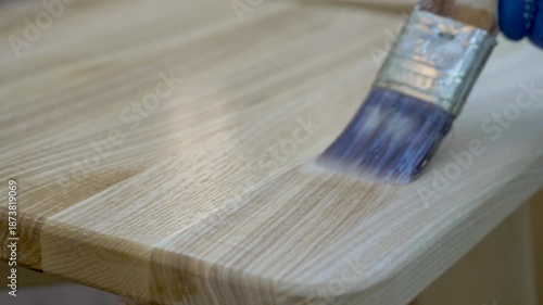 Protective enamel bonds with wooden surface as brush spreads even layer. Coating secures structure while highlighting depth, ensuring sleek and refined appearance