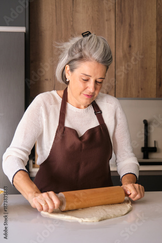 Woman rolling dough with a wooden rolling pin in a modern kitchen