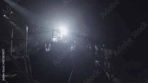 Drummer sits at drums surrounded by strong stage back lights in backstage. Darkness creates contrast during soundcheck in concert hall