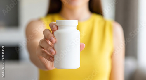 Woman holding white supplement bottle in hand, wearing bright yellow top, showcasing health and wellness concept with focus on nutrition