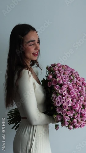 A vertical shot shows a young woman in white lounge wear holding a giant, lush bouquet of pink roses. This romantic image is perfect for Valentine's Day or anniversary themes.