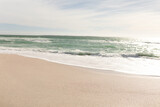 Waves in sea crashing on shore at beach against sky during sunny day